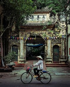 a woman riding a bike down a street next to a tall building with an archway