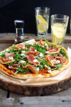 a pizza sitting on top of a wooden cutting board next to glasses and lemonade