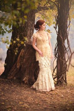 a woman standing in front of a tree trunk wearing a dress with ruffles