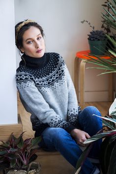 a woman is sitting on the floor next to some potted plants and wearing a sweater