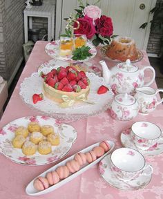 a pink table topped with plates and cups filled with food next to a basket of strawberries