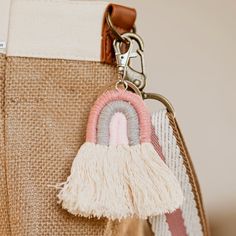 a purse with a key chain attached to it's side and a pink, white, and grey tassel hanging from the front