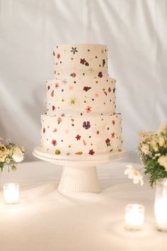 a wedding cake with flowers and candles on the table in front of white linens