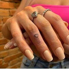 a woman's hand with a small heart tattoo on her left thumb and finger