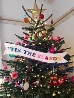 a christmas tree decorated with ornaments and ribbon that says tis the season hanging on it