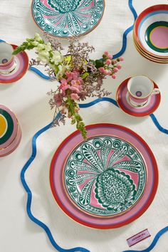 the table is set with colorful plates and flowers in vases on top of it