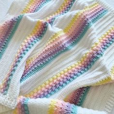 a crocheted sweater laying on top of a bed next to a white blanket