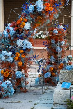 an arrangement of blue and orange flowers on display in front of a brick building with columns