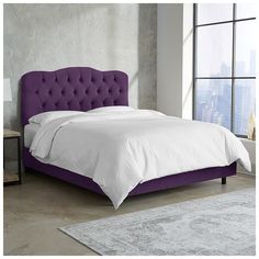 a bed with a purple headboard and white sheets in a room next to a window