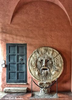 a stone lion head is on display in front of a red stucco wall with an arched doorway