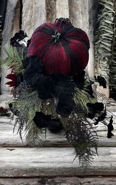 a red pumpkin sitting on top of a wooden table next to black flowers and greenery