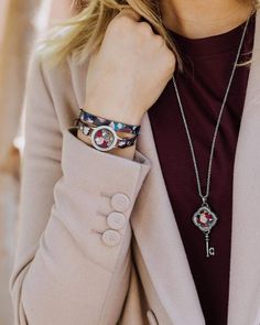 a woman wearing a necklace and jacket with a cross charm on it's wrist