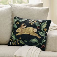 a black and gold pillow with a rabbit on it sitting on a couch next to a window