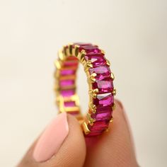 a woman's hand holding a gold ring with pink stones on the inside and outside