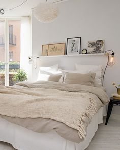 a bed with white linens and pillows in a bedroom next to a lamp on a table