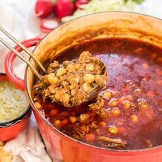 a red pot filled with chili and beans next to other food on a white table