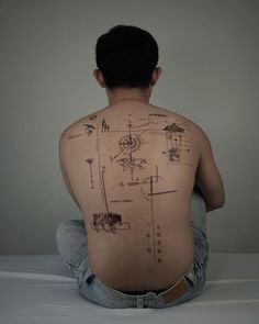 a man sitting on the floor with his back to the camera and drawings all over him