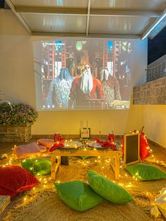 a large screen in a room with pillows on the floor and lights all around it