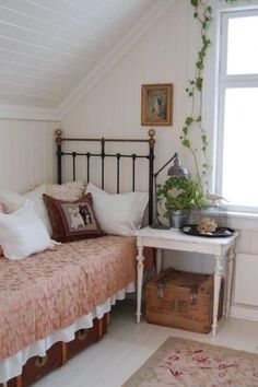 a bed sitting under a window next to a wooden table with a potted plant on top of it