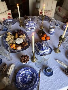 a table set with blue and white plates, silverware, candles and other items