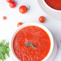 two white bowls filled with tomato soup and garnished with basil leaves on the side