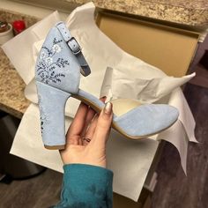 a woman is holding up her blue high heeled shoes with flowers on the side