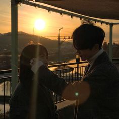 a man and woman standing next to each other near the sun in the sky at sunset