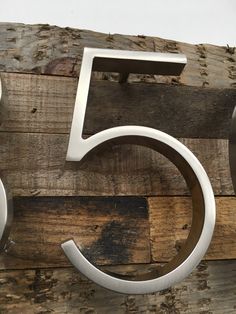 the number five is made from metal and sits on a wooden planked wall,