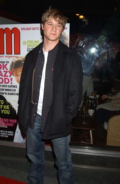 a young man standing on top of a red carpet next to a magazine cover at night