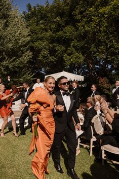 a man and woman in formal wear walking down the aisle at an outdoor wedding ceremony