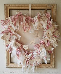 a heart shaped wreath hanging on the wall in front of a frame with tags attached to it