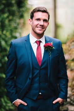 a man in a blue suit and red tie smiles at the camera with his hands in his pockets