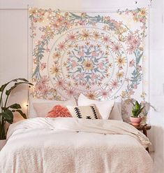 a white bed topped with lots of pillows next to a wall covered in floral tapestry