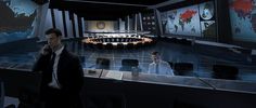 a man standing in front of a desk with two monitors on the wall behind him