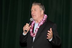 a man in a suit holding a microphone and wearing a flower lei around his neck