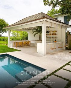 an outdoor kitchen with a pool in the foreground and green grass on the other side