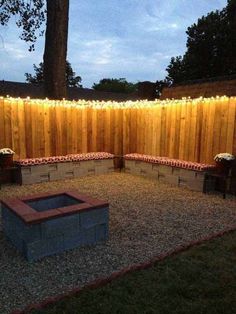 an outdoor fire pit in the middle of a yard with string lights strung around it