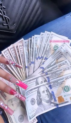 a woman's hand holding money in her lap with pink nail polish on it