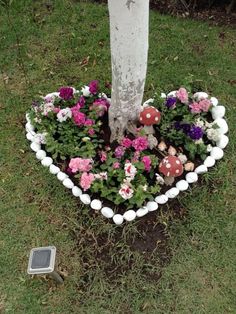 a heart shaped planter with mushrooms and flowers in the grass next to a tree