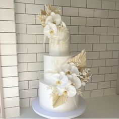 a three tiered cake with white flowers on top and gold leaf decoration around the edges