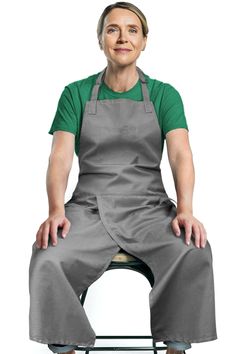 a woman sitting on top of a stool wearing an apron and grey pants with her legs crossed