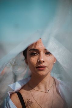 a woman with freckles on her face is looking at the camera through a veil