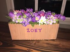 a wooden box filled with purple and white flowers on top of a wooden floor next to a window