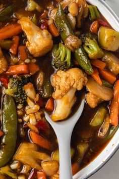 a spoon full of vegetables and meat in a stew with broccoli, cauliflower, carrots