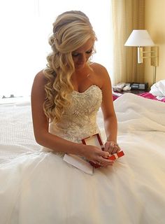 a woman sitting on top of a bed in a wedding dress holding a red box