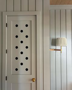 a white door with black flowers painted on the side and a wall lamp next to it