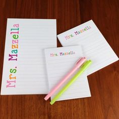 two notepads and a pen sitting on top of a wooden table next to each other