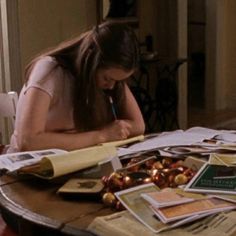 a woman sitting at a table with papers and pens in her hand, writing on a piece of paper