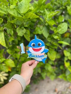 a hand holding up a small blue toy with a shark on it's face