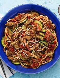 a blue bowl filled with spaghetti and meatballs on top of a table next to two forks